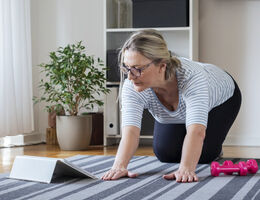 A woman in a living room follows a fitness routine on her tablet.