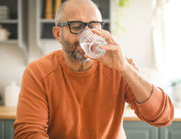 An older man drinks a glass of water.