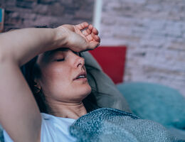 A woman in bed with an arm across her forehead.