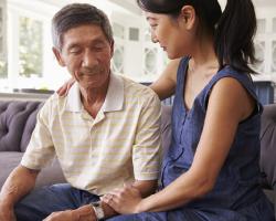 A woman comforts an older man as they sit on a couch